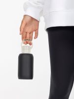 Botella de entrenamiento Squat sostenida por el asa, junto a leggins negros.