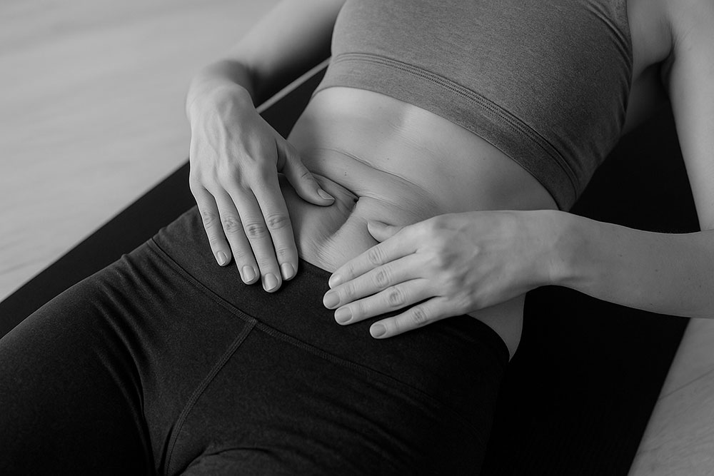 Mujer en postparto mostrando con las manos la separación abdominal típica de una diástasis sobre esterilla de ejercicio