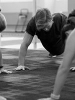 Personas realizando flexiones en grupo durante una sesión de entrenamiento funcional en interior, con apoyo de manos sobre el suelo.