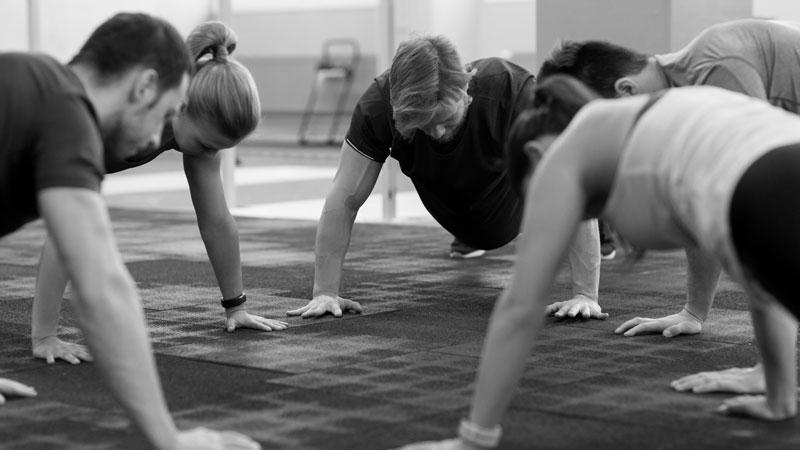 Personas realizando flexiones en grupo durante una sesión de entrenamiento funcional en interior, con apoyo de manos sobre el suelo.