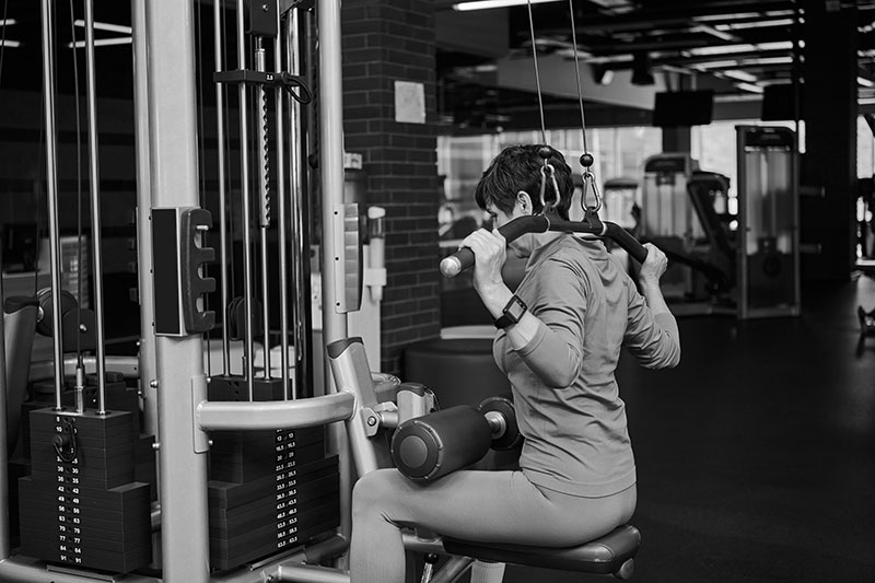 Persona realizando ejercicio de fuerza en máquina de gimnasio, trabajando espalda y hombros con polea sentada.